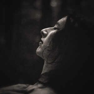 Picture of a woman with her arms on her chest and eyes closed who is relaxing in the dark woods. Source Pixabay.com.