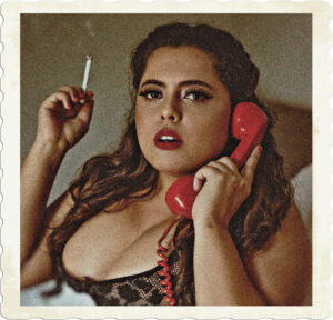 Picture of a round faced brunette with a large bust, wearing lingerie, has a cigarette in one hand, and a corded phone in the other. Picture by Marlon Alves on Pexels.