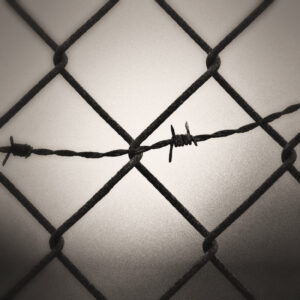 Picture of a rusty chain link fence with barbed wire running through it. Source Pixabay.com.