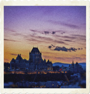 Picture of le Chateau Frontenac taken from the Levis side. Taken at or near sunset, with a crepuscular sky, the hotel itself is alight as is the palisade. Image by Emeric Laperriere from Pexels.