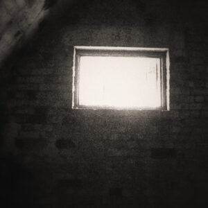 Picture of a brick wall, part of a vaulted ceiling, and a lonely window the sole source of light. Source Pixabay.com.
