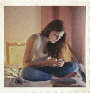 Picture of a brunette in a cluttered room focused on her phone. Image by Andrea Piacquadio on Pexels.