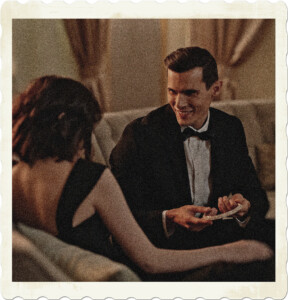 Picture of a man and woman in a ritzy locale, man is wearing a tuxedo, woman a dark formal dress. He appears to be holding an elaborate hairband. Image by cottonbro studio from Pexels.