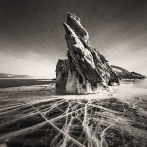 Image of a rock protruding from a frozen lake, with visible cracks in the ice. Source Pixabay.com.