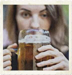 Picture of a glass mug of beer, with a blurred woman in the background eyeing her drink. Image by Engin Akyurt from Pixabay.