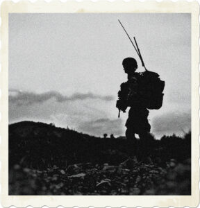 Picture of a lone soldier walking along rocky terrain. Soldier is wearing a full pack with a radio. Image by Amber Clay from Pixabay.