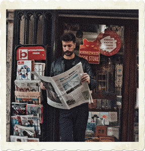 Picture of a man reading a newspaper besides a newstand. Image by Furkanfdemir from Pexels.