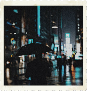 Picture focused on a gentleman holding an umbrella walking in the rain. If the background the burred lights of a city. Image by Zeeshaan Shabbir from Pexels.