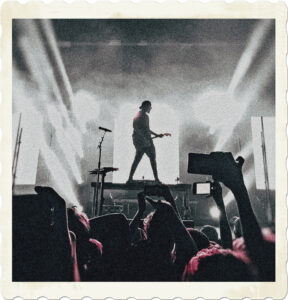 Image of a guitarist on the centre state of a stage lit up in white light. In the foreground there are spectators taking shots of the show with their cameras. Image by Sebastiaan Stam from Pexels.