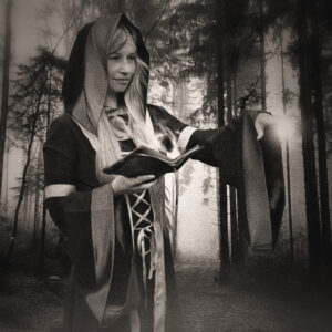 Picture of a woman in robes, holding a spellbook, and some sort of magic effect originating from outstretched hand. Source Pixabay.com.