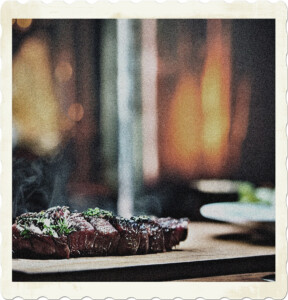 Picture of a sliced steak with seam still rising from the meat. While the cutting board is in focus, the rest of the surroundings are not. Image by Chil Vera from Pixabay.