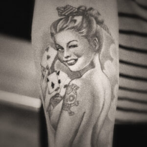 Picture of a tatoo featuring a topless woman holding cards and wearing a suggestive smile. Source Pixabay.com.