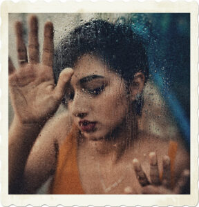 Picture of a dark haired woman pressing her hands against a wet window.  Image by Edu Carvalho from Pexels.