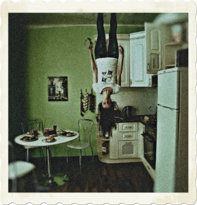 Picture of an ordinary looking kitchen, featuring a table full of food. However, a woman in jeans and a white t-shirt appears to be hanging from the ceiling. Image by Pixabay from Pexels.