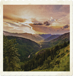 Picture of a mountainous valley, with a river running along the bottom. The cloud is concealed by the clouds, colouring the sky in yellow and orange. Image by Pexels from Pixabay.