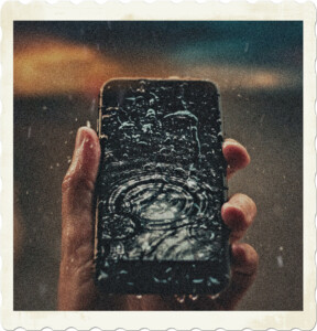Picture of someone holding a phone in the rain, screen is covered is water, with a waterdrop effect on the screen. Image by Vanderlei Longo from Pexels.