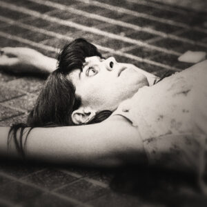 Picture of a woman laying on a tiled floor, eyes wide, look of fright. Source Pixabay.com.