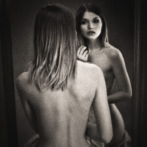 Picture of a woman from the back with her reflection visible in a mirror ahead. Source Pixabay.com.
