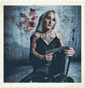 Picture of a blonde holding a weapon, dressed in black leather, hard look on her face, holding a weapon, and blood splatter on her face and walls. Image by Joakim Mosebach from Pixabay.