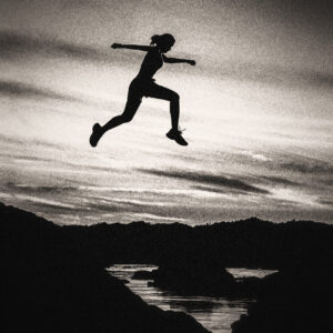 Picture of a woman leaping from one edge of a lake to another. Silhouetted against the background. Source Pixabay.com.