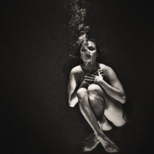 Picture of a woman in dark water, submerged, with bubbles rising above her. Source Pixabay.com.