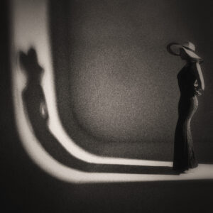 Picture of a woman in a form fitting dress and a hat, with her shadow stretching out onto the wall. Source Pixabay.com.