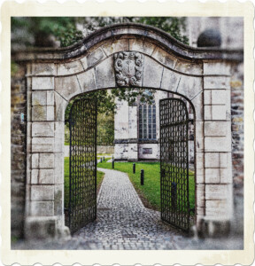 Picture of an iron gate surrounded by a stone wall, with a cobble stone pathway leading to structures in the background. Image by Peter H from Pixabay.