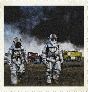 Picture of two firefighters walking away from the firetrucks in the distance. A thick plume of smoke covers the sky. Image by Pixabay on Pexels.