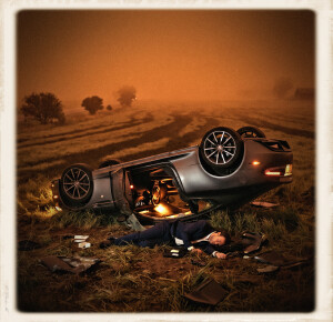 A flipped silver-gray high-end sports car rests overturned in a grassy field under thick orange fog at night, with a man in a dark blue suit lying motionless on the ground beside the wreck amid scattered debris and tire tracks stretching into the misty distance.