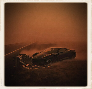 A dark luxury sports car sits crashed against a mangled metal guardrail along a desolate highway. The scene is shrouded in heavy orange dust or fog, creating a moody, monochromatic atmosphere framed by a white vintage photo border.