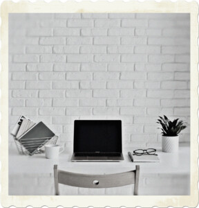 Picture of a white desk, with white attributes on it, with a white brick wall in the background. There are no real colours, creating a depressive atmosphere. Image by Karolina Grabowska from Pexels.