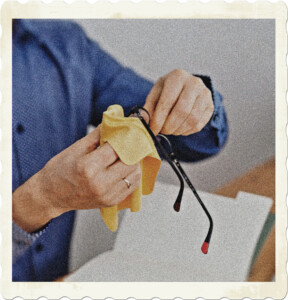 Picture of someone in a blue buttoned shirt cleaning their glasses with a cloth. Image by Karolina Grabowska from Pexels.