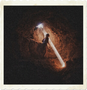 Picture of a woman walking through a tunnel. There is an opening at the end, a filament of light if shining through to the ground. Image by Brady Knoll from Pexels.