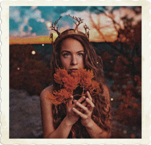 Picture of a brunette with brown eyes wearing a crown of trees, and holding a branch. Appears to be fireflies in the background, as the sun is setting. Possibly druid or goddess cosplay. Image by Roy Reyna from Pexels.