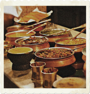 Picture focused on a long table filled with Indian food dishes, served as a buffer. Image by Public Domain Pictures from Pixabay.