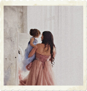 Picture of a mother and daughter taking from the back. Both are wearing formal dresses, pink and blue respectively, mother appears to be speaking to the child who is looking out a window. Image by Марина Вельможко from Pixabay.