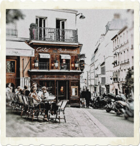 Picture of a cobbled sidewalk with tables and patrons outside of a restaurant. Mopeds are parked up front, and the neighbourhood has a European feel to it. Image by Rachel Claire from Pexels.