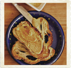 Picture of two pieces of home made bread on a blue plate. A white spread is over the top piece, which also covers the top part of the knife leaning against the plate. Image by Kim van Vuuren from Pexels.