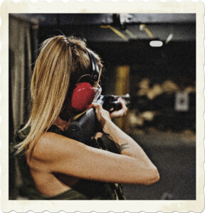 Woman with long blond pony tail, red ear defenders, and a ballistic vest pointing a shotgun down range at a target. Image by Karolina Grabowska from Pexels.