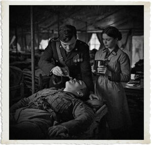 Highly detailed cinematic scene inside a dimly lit canvas ward tent at a British Casualty Clearing Station during the Great War in 1915. A distinguished British Colonel named Marc gently props up a severely wounded soldier named Mackenzie in his cot and brings a glass of water to the man's feverish lips. The soldier drinks greedily, as though dying of thirst after forty days in the desert, his eyes half-open in desperate relief. The Colonel carefully supports the soldier's head and shoulders with one arm while holding the glass steady with the other. Standing close by is a young Canadian Bluebird nurse, a brunette with lively steel-grey eyes and a mischievous grin, holding the now-empty stainless-steel pitcher and watching the scene with quiet surprise and interest. Soft moody lamplight illuminates the intimate moment, casting dramatic shadows. In the background, rows of cots with other wounded soldiers, medical equipment, faint blood stains on bandages, and the muddy war-torn atmosphere visible through the tent flaps. Historical accuracy with subtle supernatural tension from the Colonel's vampiric aid, realistic yet slightly stylized, focus on the Colonel helping the soldier drink while the nurse observes attentively. Clothing and settings appropriate for 1915.