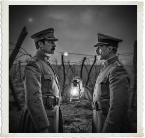 Black and white dramatic image of two World War I-era officers standing face-to-face in a tense nighttime conversation. The officer on the right holds up a glowing lantern between them, illuminating their serious expressions. The desolate battlefield background features barbed wire, broken posts, and a full moon in the cloudy sky.