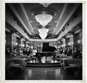 a cinematic photo of a massive Art Deco lounge with a long polished wooden bar along one wall, adorned with elegant bronze fixtures, luxurious booths with plush velvet seats, and a grand concert piano at the centre on a raised stage with intricate carvings, set against a backdrop of ornate plasterwork and crystal chandeliers, with patrons and staff dressed in formal attire suitable for 1915 Canada, including suits, hats, and elaborate dresses, captured in a warm and inviting photography style with soft lighting and rich textures.