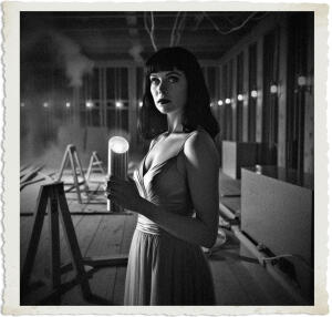 Picture of a black haired woman with green eyes wearing a slip, holding a silver cylinder in her hand that glows blue. Located in a ballroom under construction and mostly empty except for a few sawhorses, tables, and a large granite piece. The walls were still slats of wood running horizontally and in parallel. The workers had yet to apply plaster. Cabling protruded from openings in the walls and ceiling, none of it was connected. Several lanterns to chase away the darkness. The air was thick with smoke. Scene and clothing appropriate for 1915 Canada at night.
