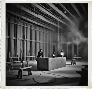 Located in a ballroom under construction and mostly empty except for a few sawhorses, tables, and a large granite piece. The walls were still slats of wood running horizontally and in parallel. The workers had yet to apply plaster.
While cabling protruded from openings in the walls and ceiling, none of it was connected. Evelyn had to use several lanterns to chase away the darkness. The air was thick with smoke. Scene and clothing appropriate for 1915 Canada at night.
