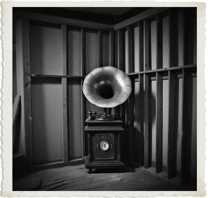 In the corner of the room there was a phonograph, an older crank style model with a horn. Ballroom under construction was mostly empty, with the wooden frame and horizontal slats in place but no plaster or windows. Scene and clothing appropriate for 1915 Canada at night.