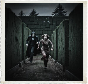 Picture of a woman running down a large hedge maze, the walls too high to scale, the scene dark, clothes bloody and torn. Chasing her is a vampire, as though the stuff of nightmares. Scene and clothing appropriate for 1915 Canada at night.