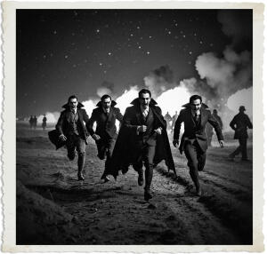 Black and white dramatic image of four men dressed as classic vampires — wearing dark suits, ties, and flowing capes with high collars — running directly toward the viewer across a smoky, war-torn battlefield at night. Their faces show intense, open-mouthed expressions as they charge forward. Explosions and bright flames illuminate the dark background, with silhouetted figures visible in the distance. The photo has a vintage aged white border.