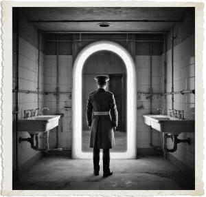 Black and white dramatic photograph of an officer in a long military greatcoat and peaked cap standing with his back to the viewer in the center of an old, tiled washroom. He faces a large, brightly glowing arched doorway that creates an eerie portal-like effect. Vintage sinks with exposed plumbing line both walls under dim overhead lighting, giving the scene a stark, mysterious, and slightly unsettling atmosphere