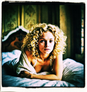 Picture of a blonde with curly hair and round cheeks waking up from bed without clothes. Stretches her arms. Located a simple bedroom. Clothes and scene appropriate to the 16th Century France.