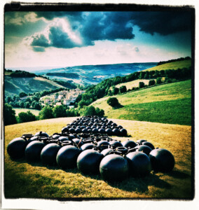 Ten large black bombs with fuses rolling down a hill. Background and clothes appropriate for 16th century France.